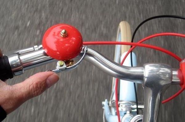 A hand ringing a red brass bicycle bell on the handlebar